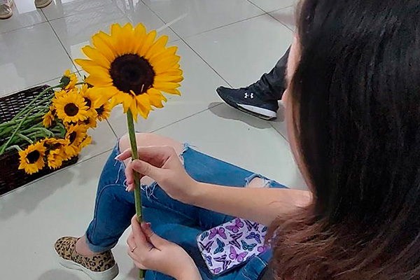 La imagen muestra una adolescente con una flor en la mano